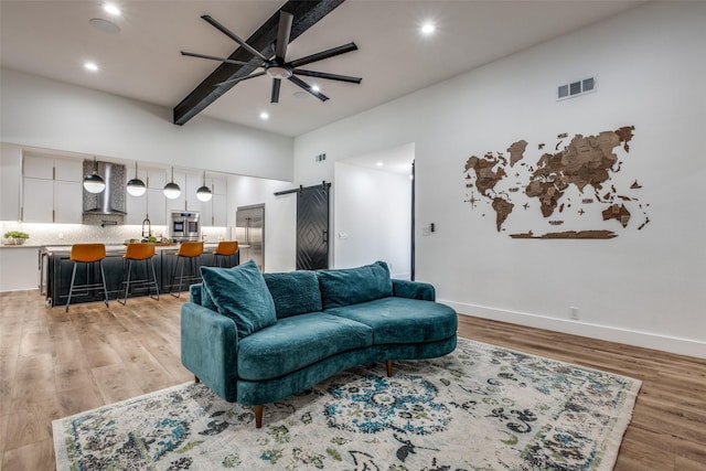 living area with light wood-type flooring, a barn door, and beamed ceiling