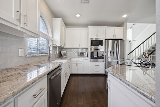 kitchen featuring stainless steel appliances, white cabinets, a sink, and light stone counters