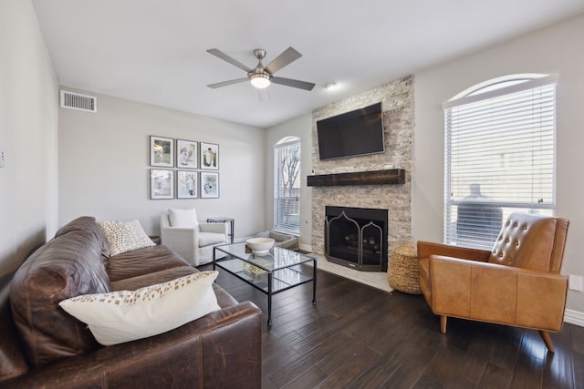 living area featuring visible vents, baseboards, dark wood-style floors, ceiling fan, and a stone fireplace