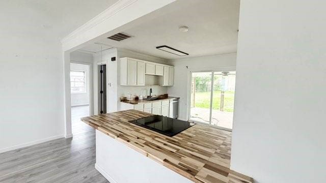 kitchen with black electric cooktop, a sink, white cabinetry, stainless steel dishwasher, and light wood-type flooring