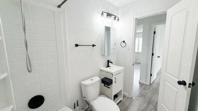 full bath featuring a tile shower, vanity, toilet, and wood finished floors