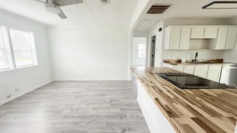 kitchen featuring visible vents, light wood-style flooring, a sink, ceiling fan, and baseboards