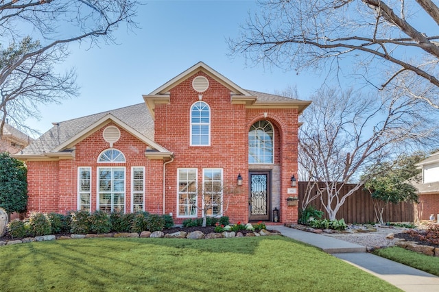 traditional home featuring roof with shingles, fence, a front lawn, and brick siding