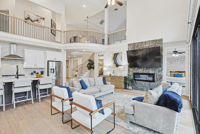 living room with ceiling fan, light wood-style flooring, a fireplace, visible vents, and stairs