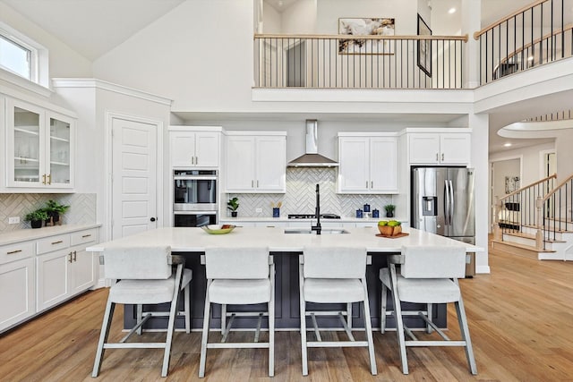 2840 Killdeer Trl, Prosper, TX 75078 - kitchen with wall chimney exhaust hood, stainless steel appliances, a high ceiling, white cabinetry, and a center island with sink