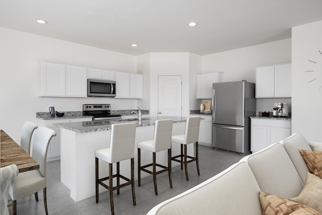 kitchen with appliances with stainless steel finishes, white cabinetry, a center island with sink, and a kitchen breakfast bar