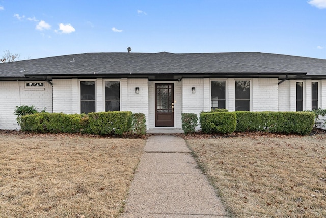 single story home featuring a shingled roof, a front lawn, and brick siding