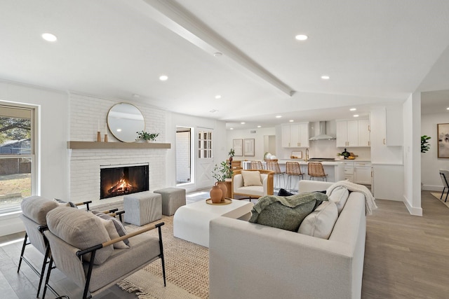 living room featuring lofted ceiling with beams, recessed lighting, a fireplace, baseboards, and light wood-type flooring