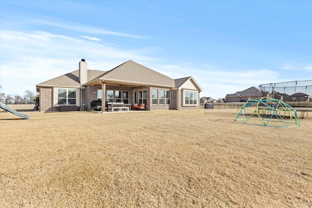 back of property featuring a chimney, fence, a playground, and brick siding