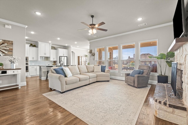 living area featuring visible vents, dark wood-style floors, ceiling fan, crown molding, and a fireplace