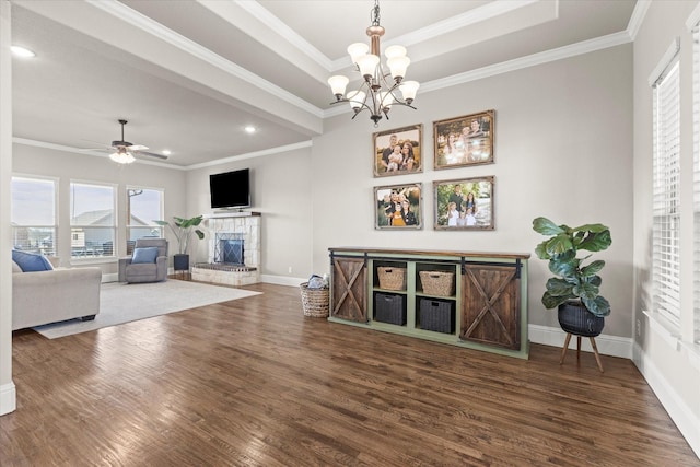 living area with a tray ceiling, crown molding, a stone fireplace, and wood finished floors