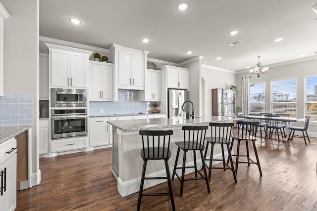 kitchen with arched walkways, a kitchen island with sink, stainless steel appliances, dark wood-type flooring, and white cabinets