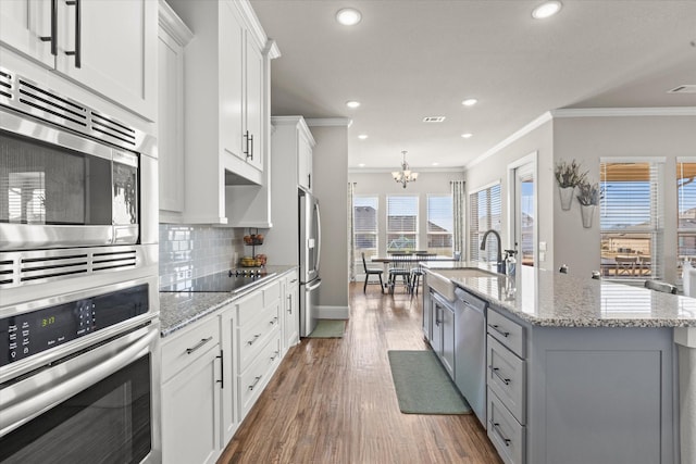 kitchen with a center island with sink, decorative backsplash, stainless steel appliances, crown molding, and white cabinetry