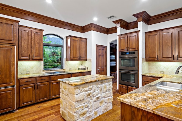 kitchen featuring visible vents, double oven, a sink, light stone countertops, and hardwood / wood-style flooring