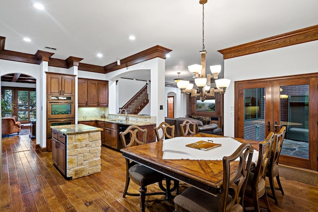 dining space with crown molding, arched walkways, dark wood finished floors, and an inviting chandelier