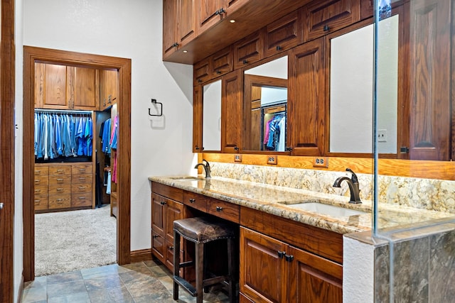 full bath with double vanity, stone finish floor, a walk in closet, and a sink