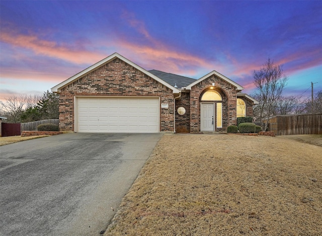 ranch-style house with driveway, brick siding, an attached garage, and fence