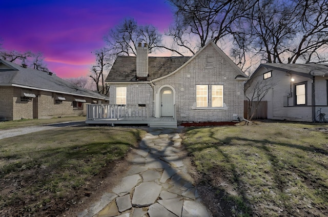 view of front of house featuring a deck, brick siding, a chimney, and a front lawn