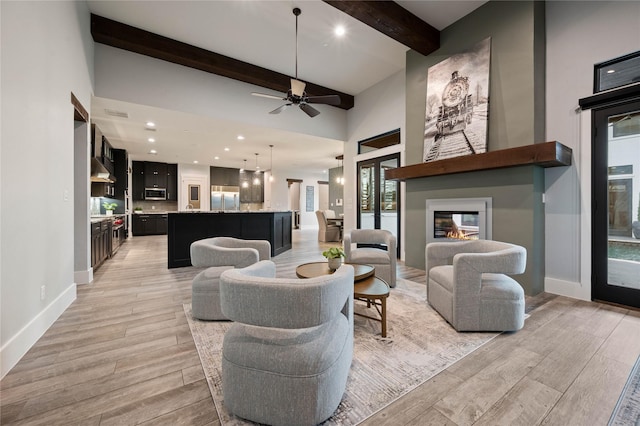 living area with a high ceiling, a fireplace, baseboards, beam ceiling, and light wood finished floors