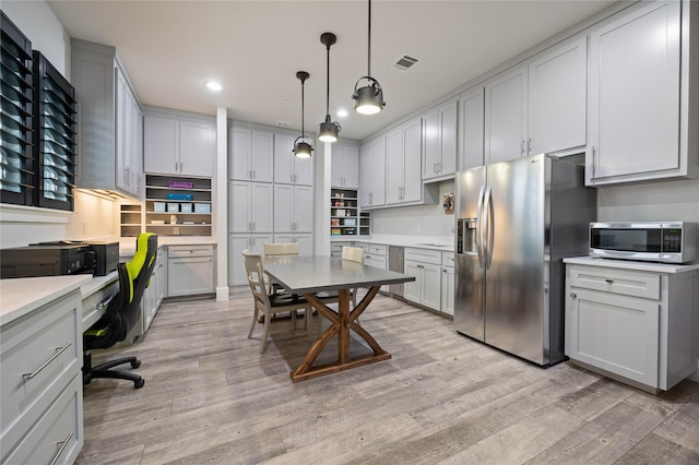 kitchen featuring built in desk, stainless steel appliances, light countertops, hanging light fixtures, and light wood-style flooring