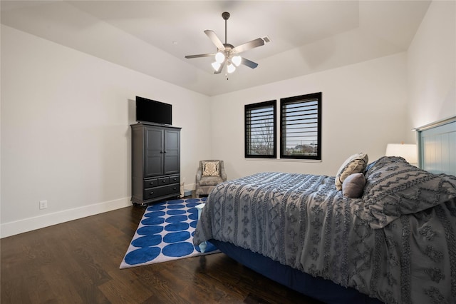 bedroom featuring dark wood-style floors, lofted ceiling, a raised ceiling, a ceiling fan, and baseboards