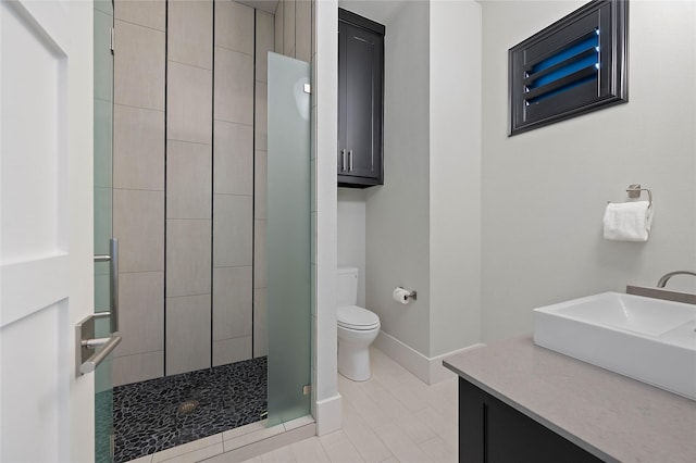 bathroom with tiled shower, vanity, toilet, and baseboards