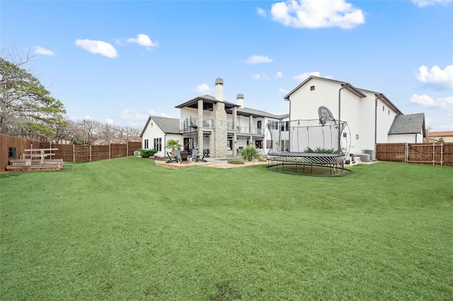 rear view of property with a yard, a trampoline, a fenced backyard, and a balcony