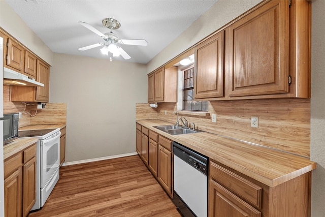 kitchen with white appliances, light wood finished floors, backsplash, under cabinet range hood, and a sink