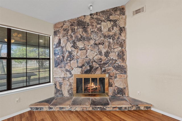 room details featuring visible vents, a stone fireplace, baseboards, and wood finished floors