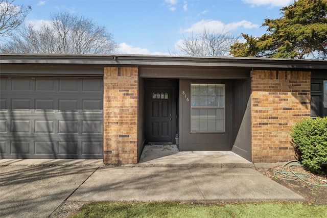 property entrance featuring a garage, driveway, and brick siding