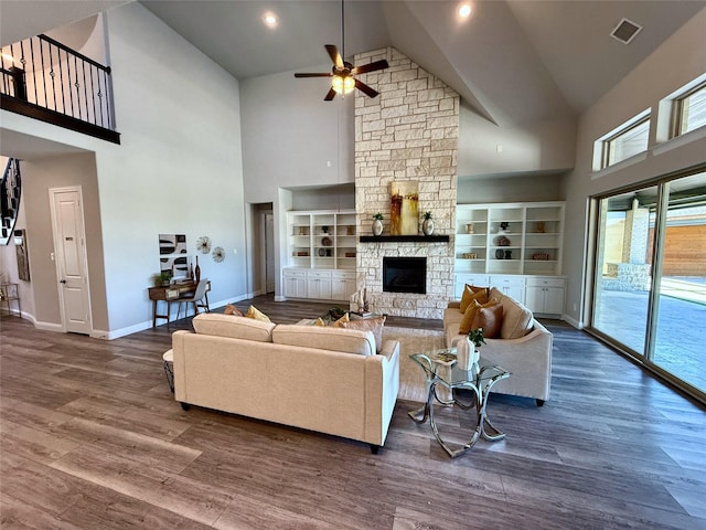 living area featuring visible vents, a stone fireplace, baseboards, and wood finished floors