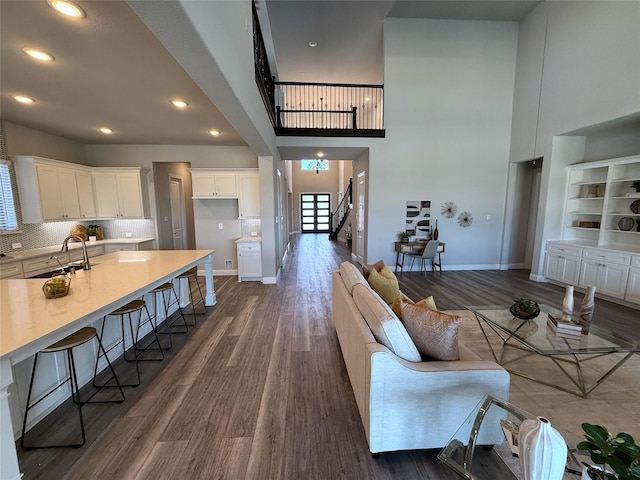 living area featuring dark wood-type flooring, stairway, baseboards, and a towering ceiling