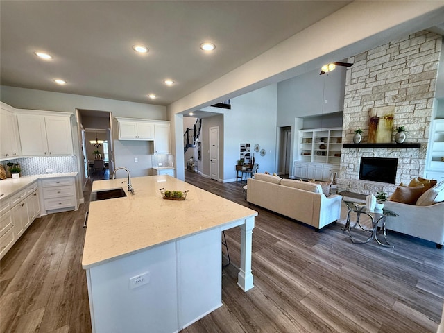 kitchen with an island with sink, a fireplace, dark wood-style flooring, a sink, and white cabinets