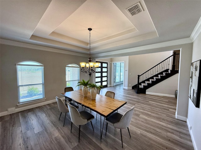 dining area with visible vents, a notable chandelier, a tray ceiling, wood finished floors, and stairway