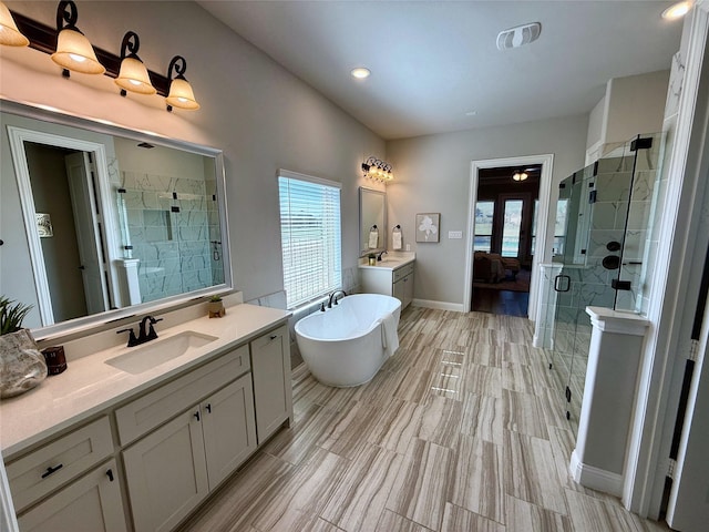 bathroom with a shower stall, a freestanding bath, two vanities, and a sink