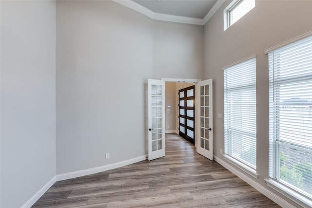 empty room featuring wood finished floors, baseboards, plenty of natural light, french doors, and crown molding