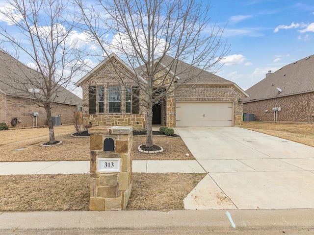 view of front of home featuring driveway, a garage, stone siding, cooling unit, and brick siding