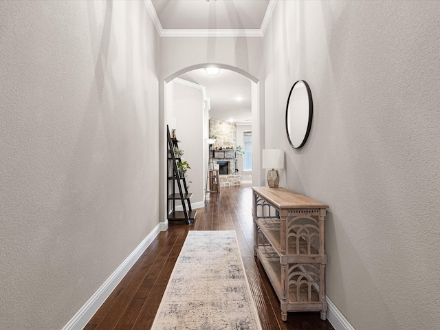 hall with dark wood-style floors, arched walkways, a textured wall, ornamental molding, and baseboards