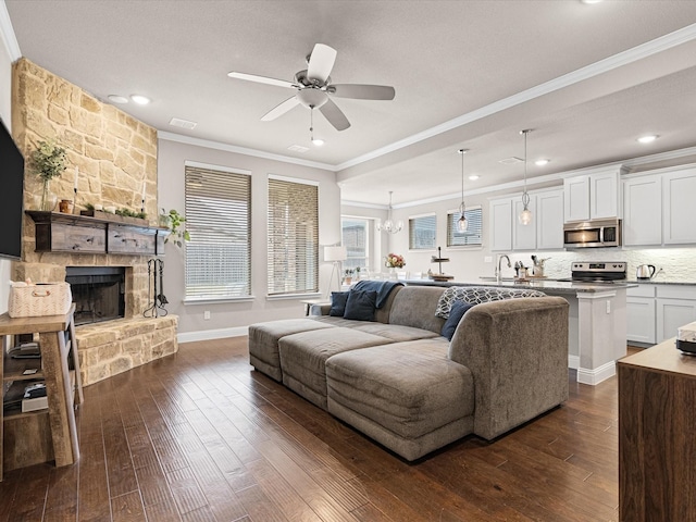 living room featuring ornamental molding, a stone fireplace, dark wood-style flooring, and ceiling fan with notable chandelier