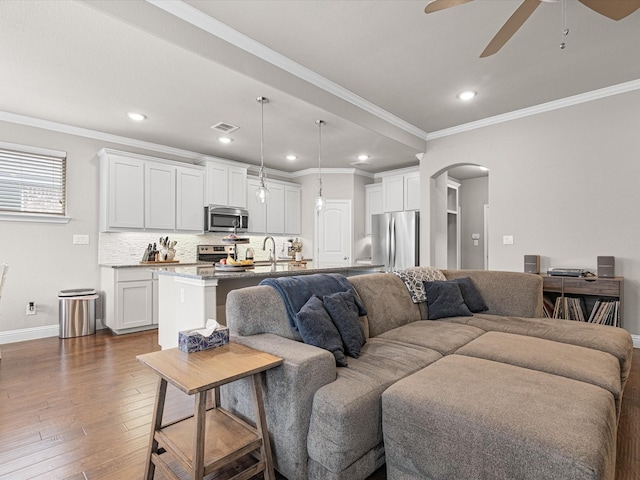 living area featuring ornamental molding, arched walkways, and dark wood-style flooring