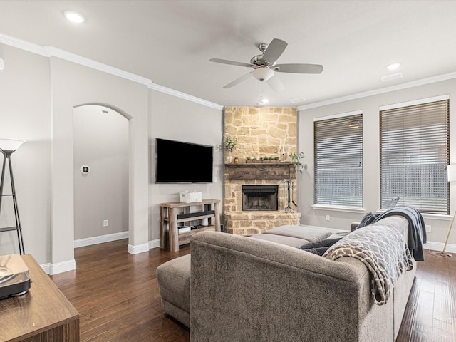 living room featuring arched walkways, dark wood-style flooring, crown molding, and a stone fireplace