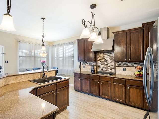 kitchen with backsplash, wall chimney range hood, freestanding refrigerator, black electric cooktop, and a sink