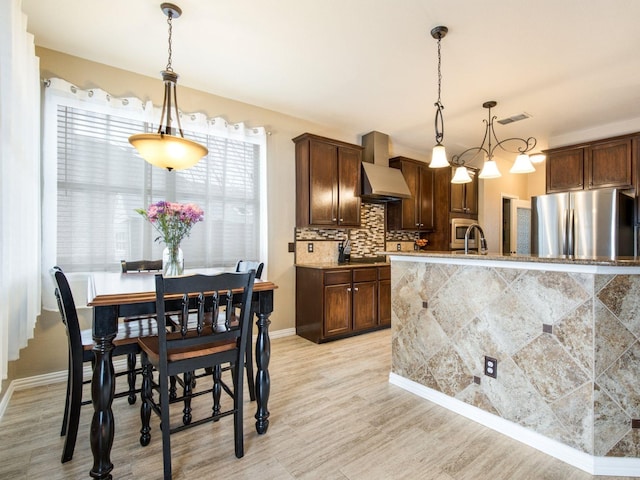 kitchen featuring light wood finished floors, visible vents, backsplash, freestanding refrigerator, and wall chimney exhaust hood