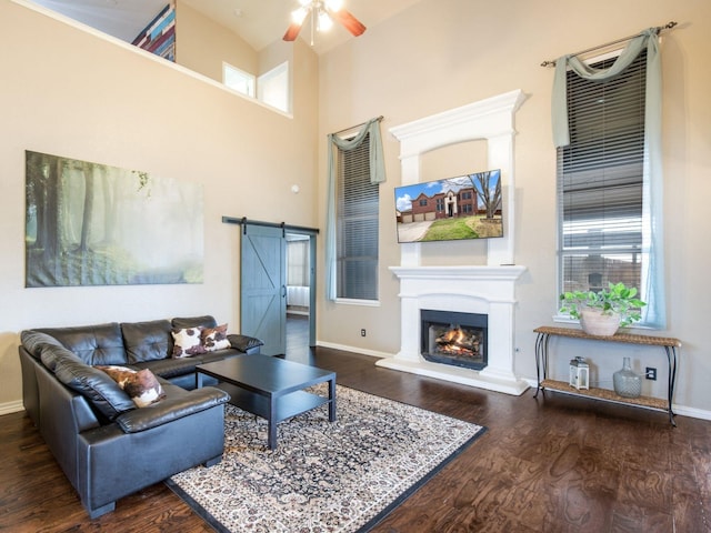 living area with a warm lit fireplace, wood finished floors, a barn door, a high ceiling, and baseboards