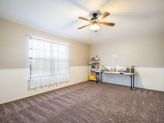 unfurnished room with carpet flooring, a ceiling fan, and wainscoting