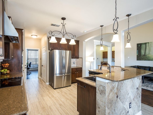 kitchen with visible vents, a sink, freestanding refrigerator, arched walkways, and black electric cooktop