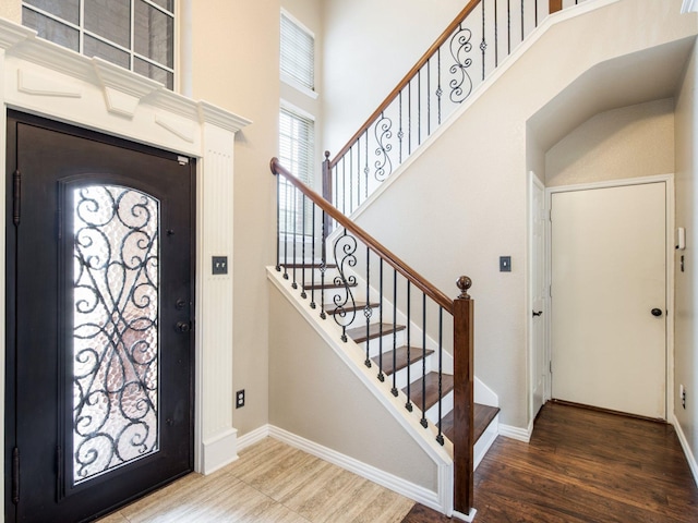 foyer with wood finished floors, baseboards, and a towering ceiling