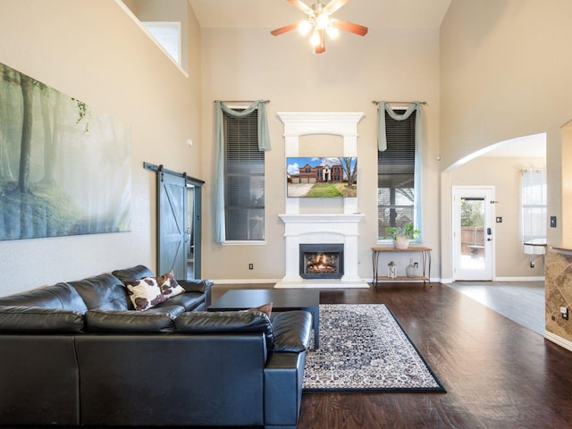 living room with a towering ceiling, a warm lit fireplace, a barn door, and wood finished floors