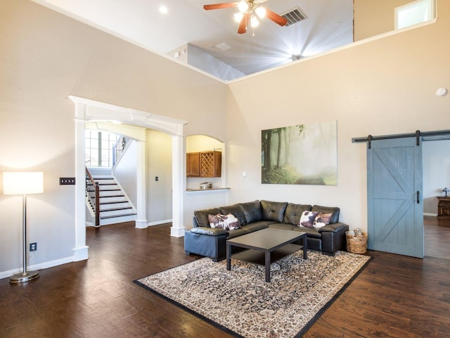 living room featuring visible vents, stairs, a barn door, a towering ceiling, and wood finished floors