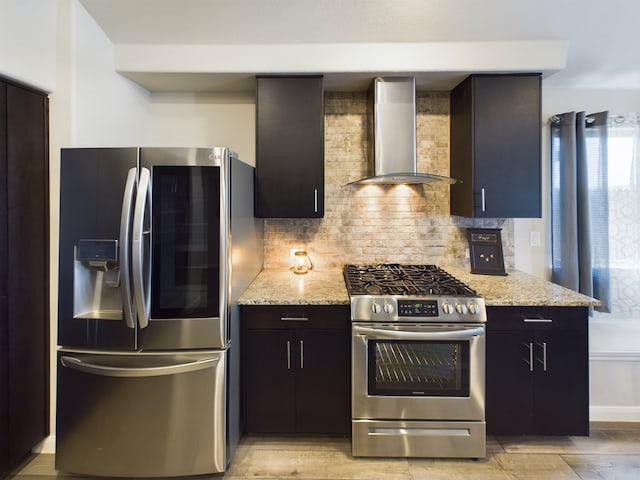 kitchen featuring stainless steel appliances, backsplash, wall chimney range hood, and light stone countertops